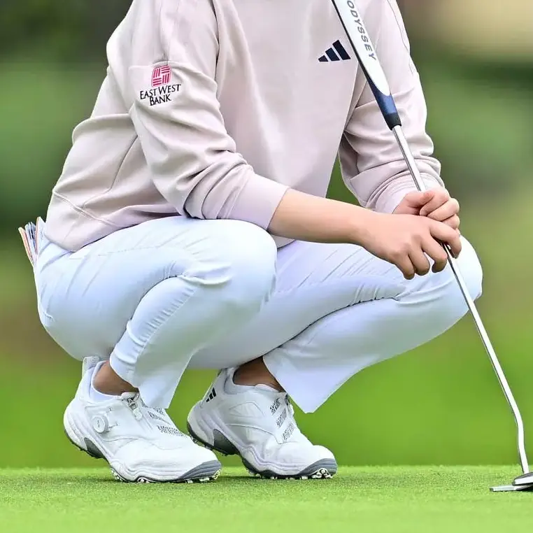 jugadora vistiendo pantalones de golf para mujer blancos, en cuclillas analizando la lectura del gree